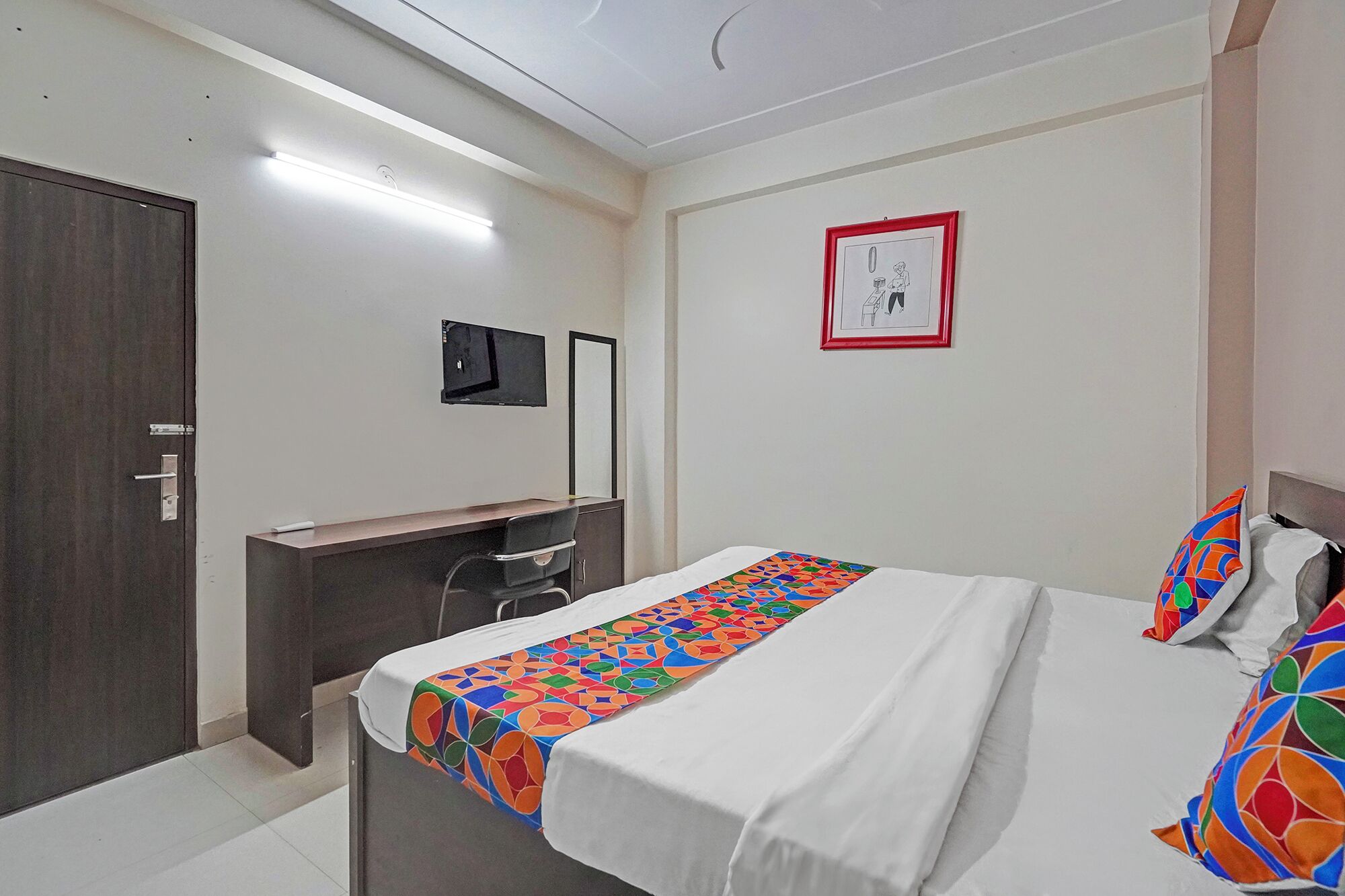 A hotel room with a bed, a desk, a chair, a TV, and a door.