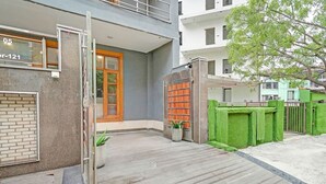 A residential building with a grey facade, a wooden door, and a small garden area with a potted plant. - Fabhotel The Virat (Noida)