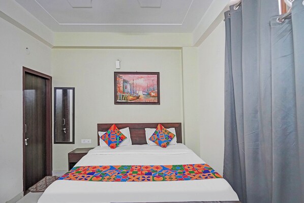 A hotel room with a bed, a nightstand, a painting on the wall, and a door. - Fabhotel The Virat (Noida)