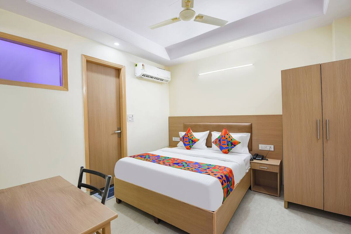 Una habitación de hotel con cama, escritorio, silla, armario y aire acondicionado.