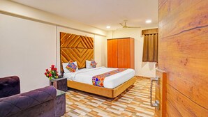 A modern bedroom with a wooden headboard, a bed with patterned bedding, a wardrobe, and a seating area with a purple sofa. - Fabhotel New Krishna Palace (Indore)