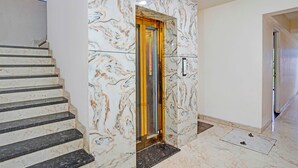 A marble staircase leading to an elevator with a glass door, surrounded by white walls and a tiled floor. - Fabhotel New Krishna Palace (Indore)