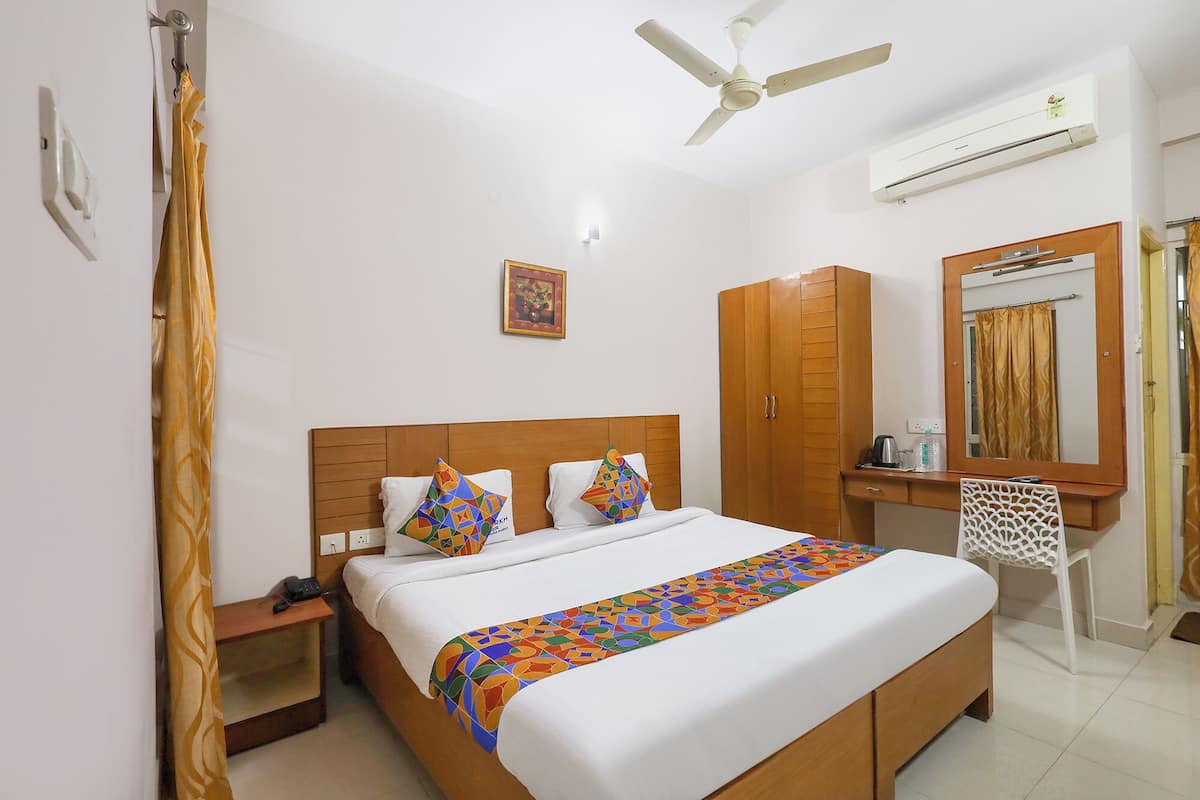 A hotel room with a bed, a desk, a wardrobe, a chair, a ceiling fan, and an air conditioning unit.