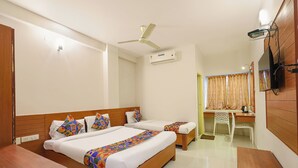 Ein Hotelzimmer mit zwei Betten, einem Schreibtisch, einem Stuhl, einem Deckenventilator, einer Klimaanlage und einem Fernseher.