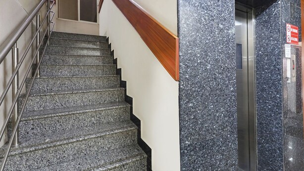 Eine Treppe mit Granitstufen und einem Holzgeländer, die zu einem Aufzug mit einer Granitwand führt.