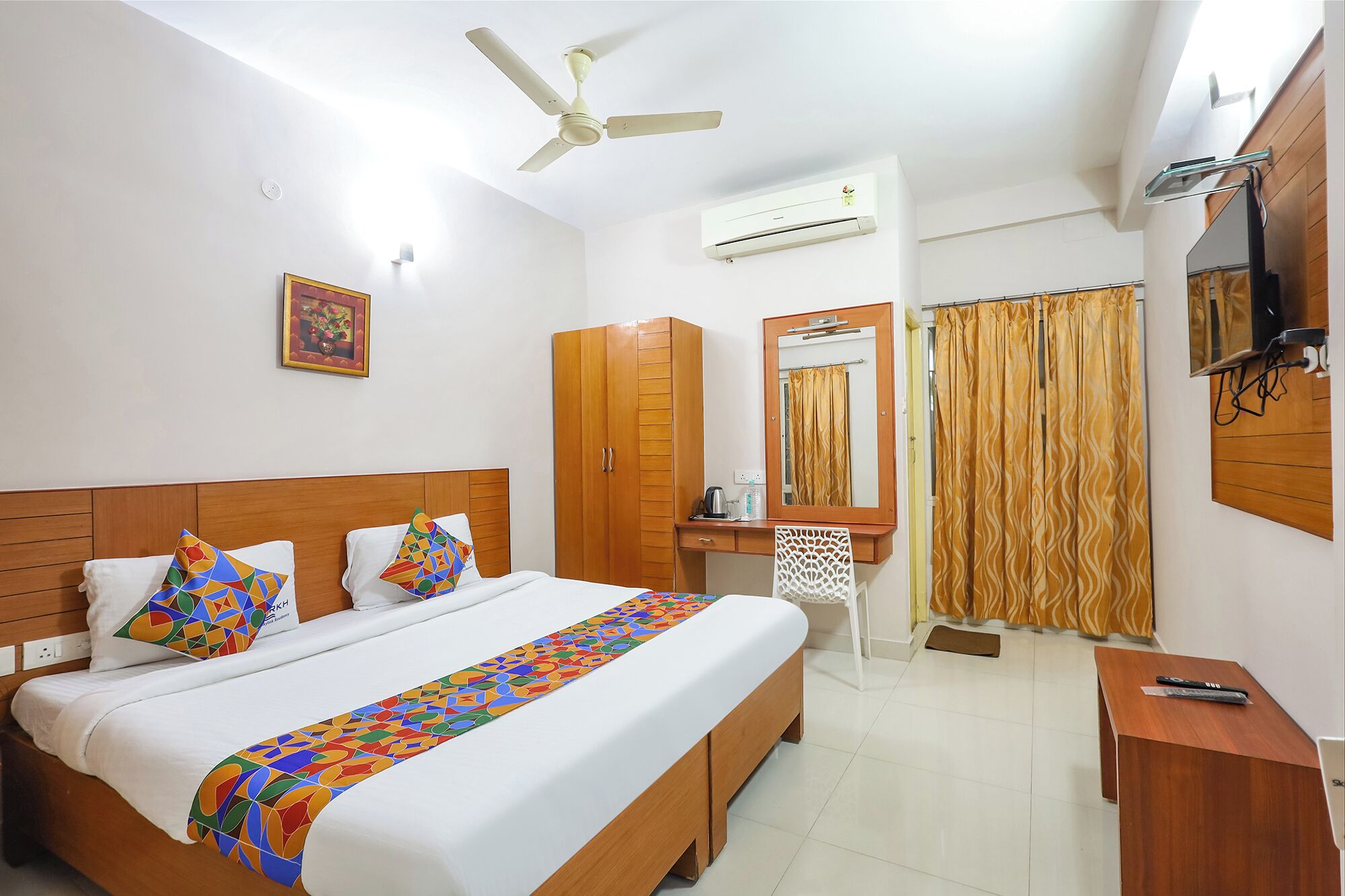 A hotel room with a bed, a desk, a chair, a wardrobe, a mirror, an air conditioning unit, a ceiling fan, and a shower curtain.