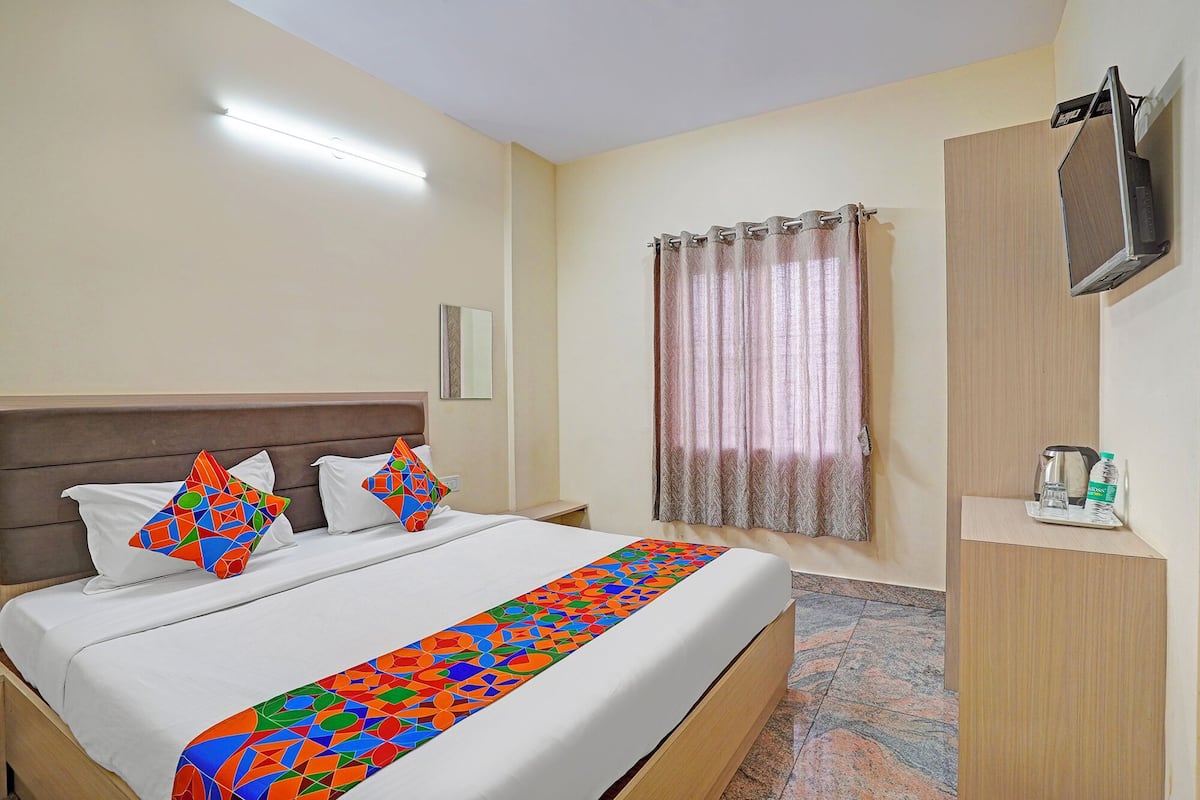 Una habitación de hotel con cama, mesita de noche, televisión, ventana con cortinas y un armario de madera.