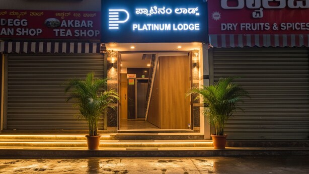 The exterior of Platinum Lodge with a neon sign, potted plants, and closed shutters on the adjacent shops. - Fabhotel Platinum (Bengaluru)