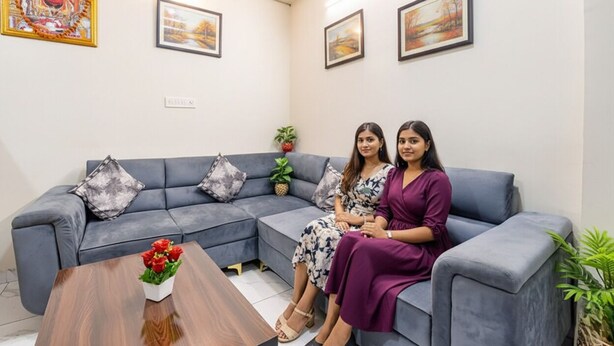 A modern living room with a grey sectional sofa, a wooden coffee table with red flowers, and framed artwork on the walls. - Fabhotel Bungalow 14 (Jaipur)
