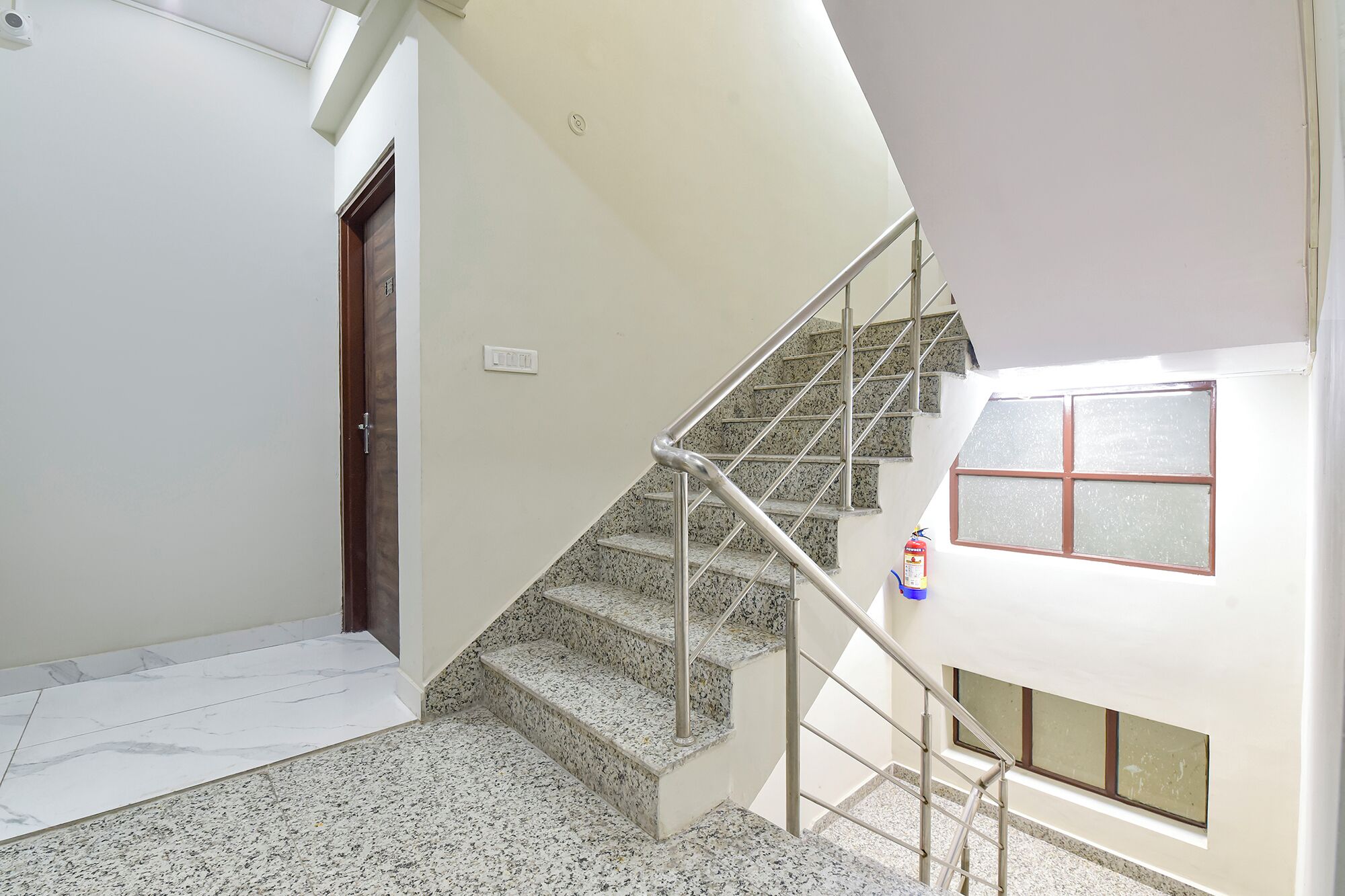 A staircase with a metal handrail, a fire extinguisher, and a window with frosted glass.