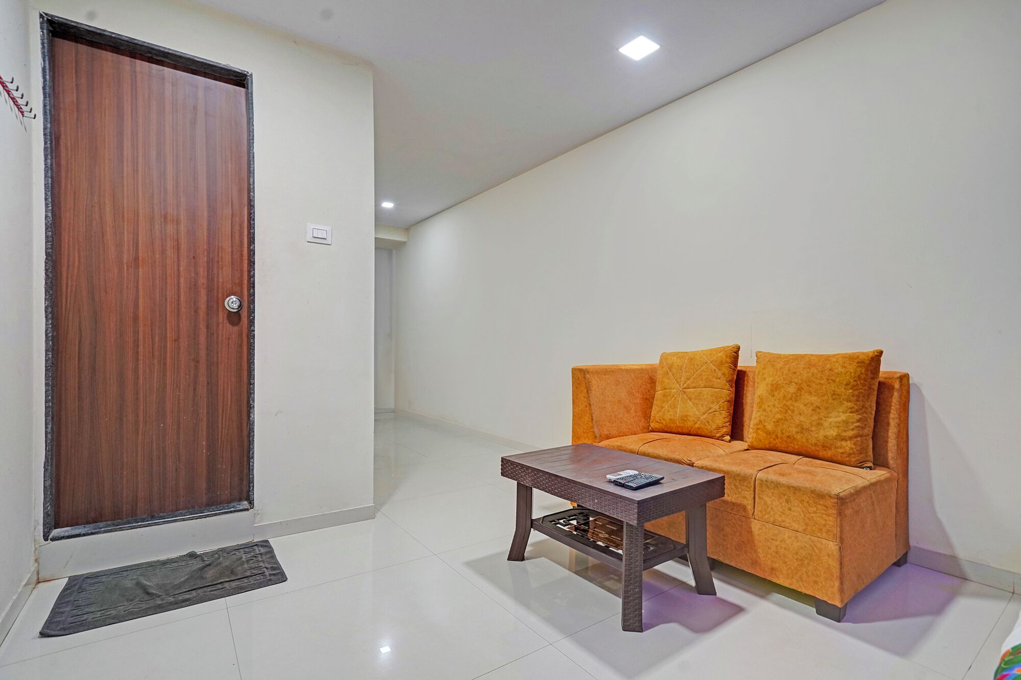 Una habitación con puerta de madera, un sofá con cojines, una mesita y un felpudo.