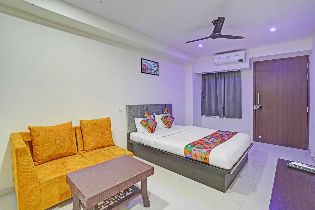 A hotel room with a bed, a sofa, a coffee table, a ceiling fan, an air conditioning unit, and a door.