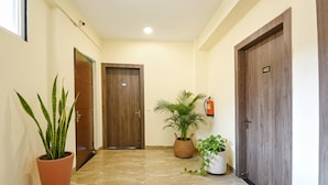 A hallway with two wooden doors, one marked with the number 402, and potted plants along the walls. - Fabhotel Alpha Stayz (Gurugram)
