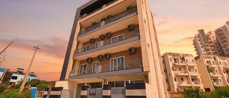 A multi-story residential building with balconies, a gated entrance, and a clear sky.