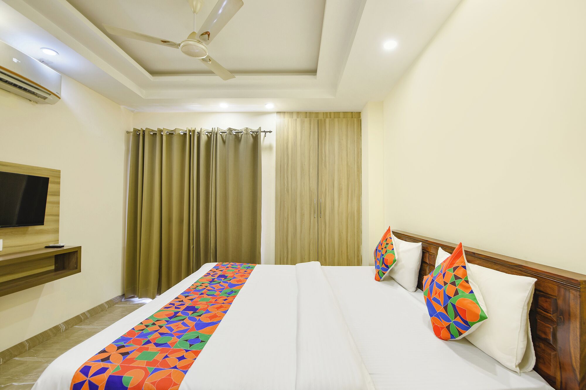 A hotel room with a bed, a TV, a ceiling fan, and curtains.