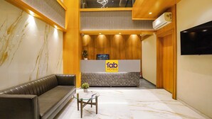 Et hotel lobby med reception, sofa, lille bord og tv ophængt på væggen.