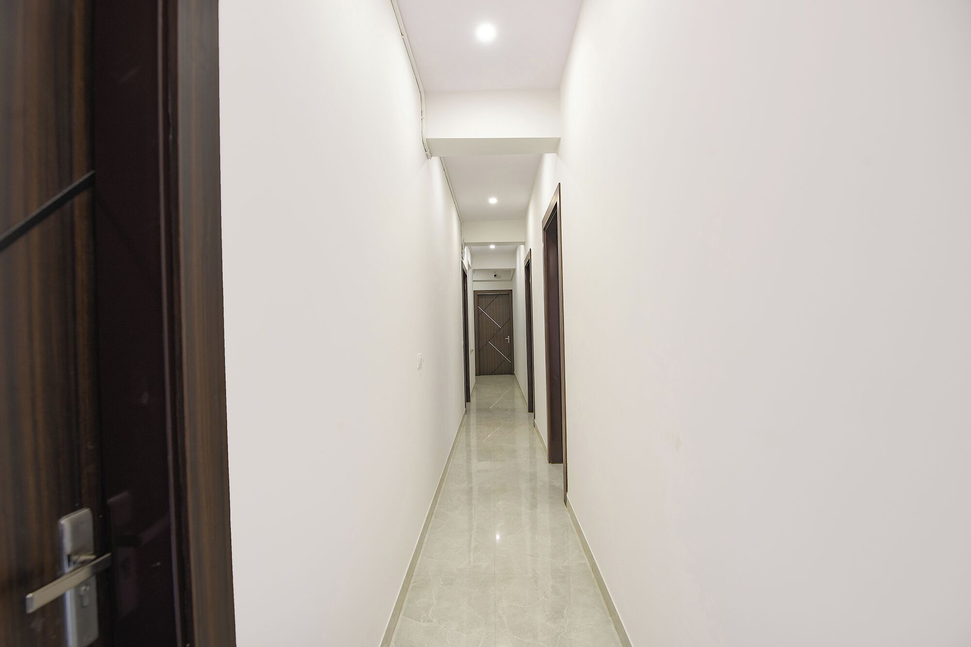 A narrow, well-lit hallway with a polished floor, leading to a door at the end.