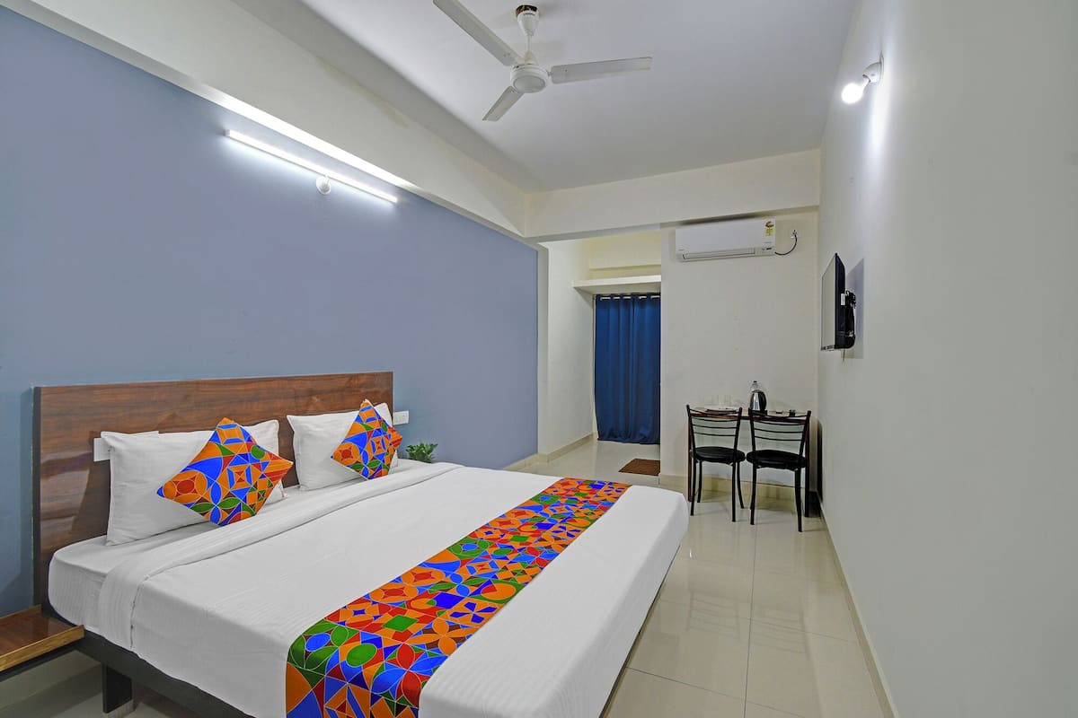 A hotel room with a bed, a ceiling fan, a TV, and a small table with chairs.