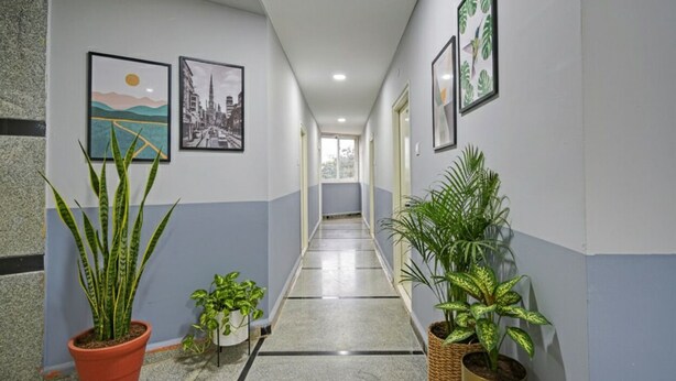 A hallway with framed artwork, potted plants, and a tiled floor. - Fabhotel Smart (Hyderabad)