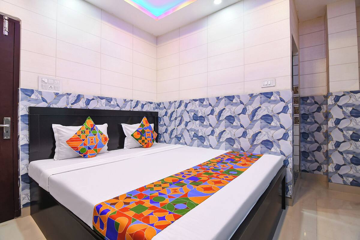 Une chambre d’hôtel avec un lit, deux oreillers, une couvre-lit à motifs et un mur décoratif aux motifs bleus et blancs.