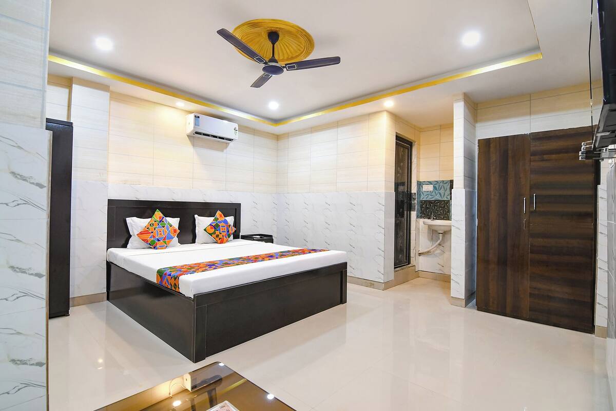 Une chambre moderne avec un grand lit, un ventilateur de plafond, un appareil de climatisation et une salle de bain équipée d’un lavabo et d’un miroir.