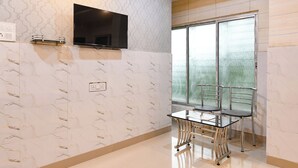 A modern room with a flat-screen TV mounted on the wall, a glass table with chairs, and a large window with frosted glass panels. - Fabhotel Top 22 (Kolkata)