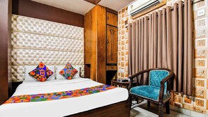 Une chambre d’hôtel avec un grand lit, une tête de lit en bois, un fauteuil recouvert d’un tissu bleu et un mur orné d’un papier peint à motifs.