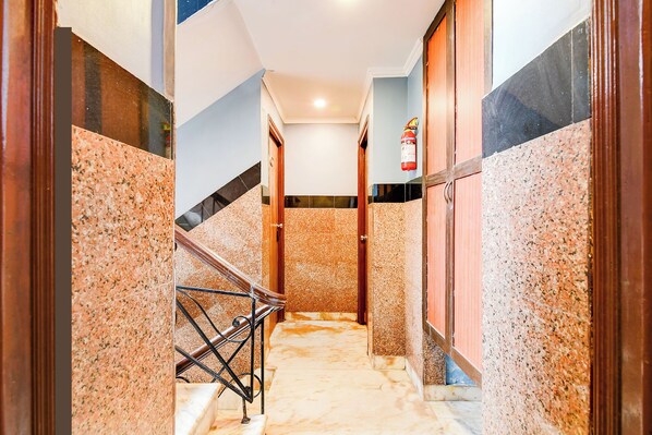 A hallway with a marble floor, wooden doors, and a fire extinguisher on the wall.