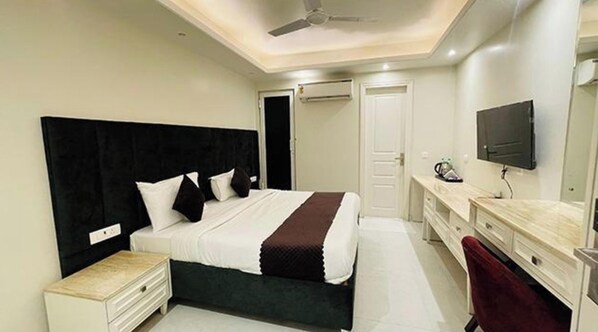 A modern hotel room with a large bed, a bedside table, a desk with a chair, a TV, and an air conditioning unit. - Fabhotel Lands Inn (Gurugram)