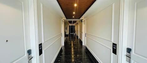 A long, narrow hallway with white walls and a black marble floor. There are doors on both sides with keypads.
