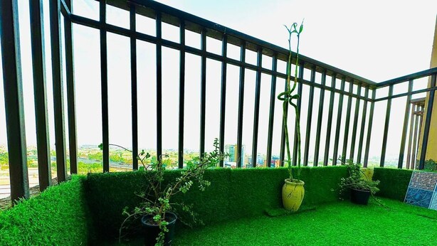 A balcony with artificial green grass, potted plants, and a metal railing. - Peaceful Escape (Zirakpur)