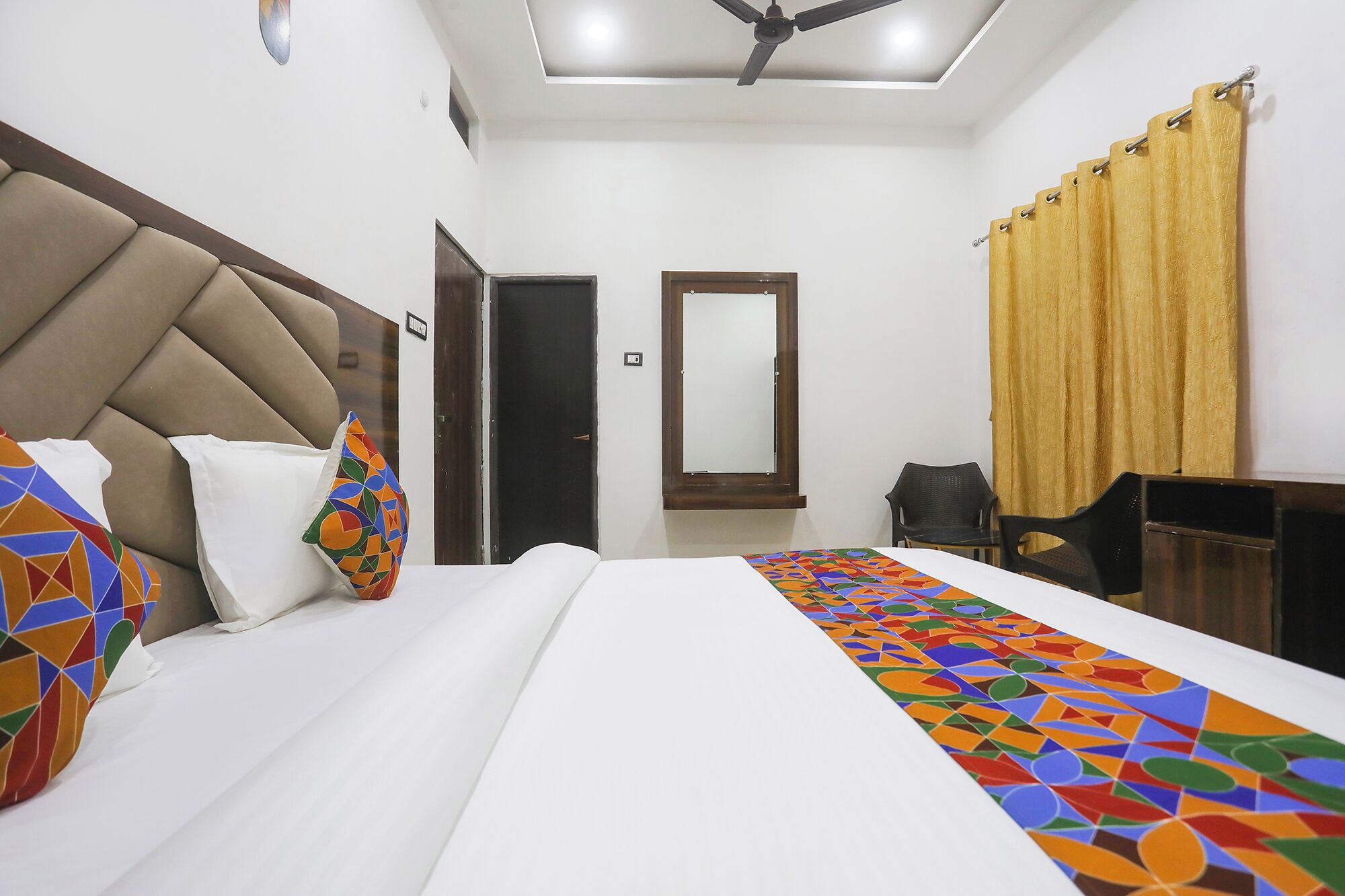 Une chambre d’hôtel équipée d’un lit, d’un bureau, d’une chaise, d’un ventilateur de plafond et d’une fenêtre avec des rideaux.
