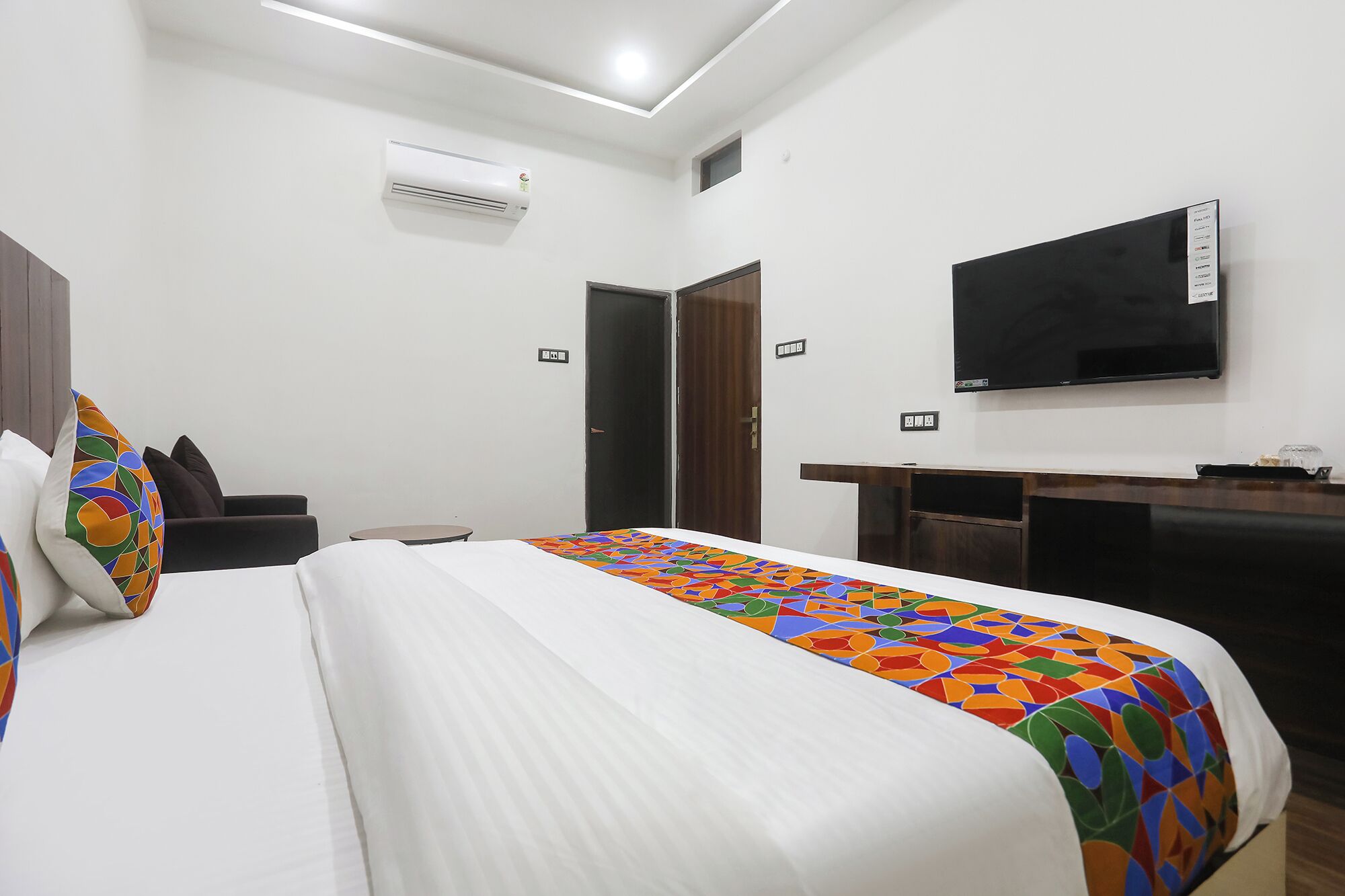 Quarto de hotel com cama, escrivaninha, televisão e ar condicionado.