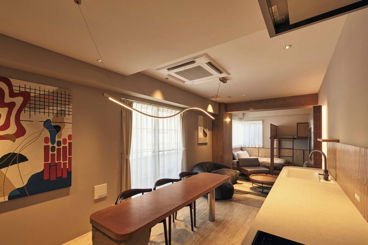 A modern hotel room with a dining area, a large window with curtains, a bed, and a bathroom with a sink and mirror.