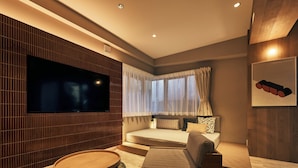 A modern hotel room with a large flat-screen TV, a sofa bed, a round coffee table, and a patterned rug. - illi Mia Kinshicho (Tokyo)