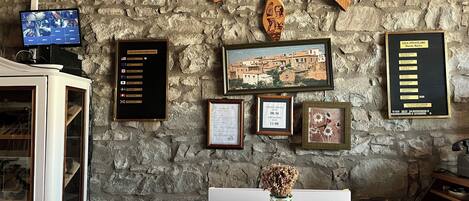 A reception desk with a stone wall background, a framed welcome sign, a framed photograph, a framed certificate, and a framed room rate sign.