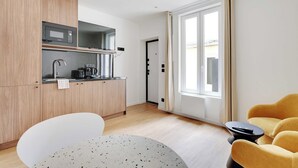 A modern kitchen with a microwave, coffee maker, and sink. There is a dining area with a white chair and a round table. A yellow armchair and a small black table are also visible. - Charming Apartment - 1BR - 2P - Montreuil (Montreuil)