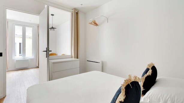 A bedroom with a bed, a bedside table, a hanging light, a window with curtains, and a door leading to another room. - Charming Apartment - 1BR - 2P - Montreuil (Montreuil)