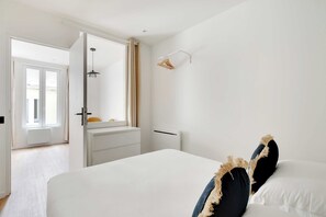 Ein Schlafzimmer mit Bett, Nachttisch, einer Hängelampe, einem Fenster mit Vorhängen und einer Tür zu einem anderen Raum.