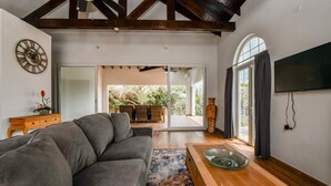 A modern living room with a grey sofa, a wooden coffee table, and a large window with curtains. - Picaron Villas (Santa Cruz)