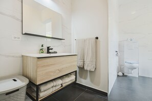 A modern bathroom with a marble wall, a wooden vanity, a toilet, and a towel rack. - Picaron Villas (Santa Cruz)