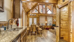 A wooden cabin interior with a kitchen, dining area, and a cozy living space.