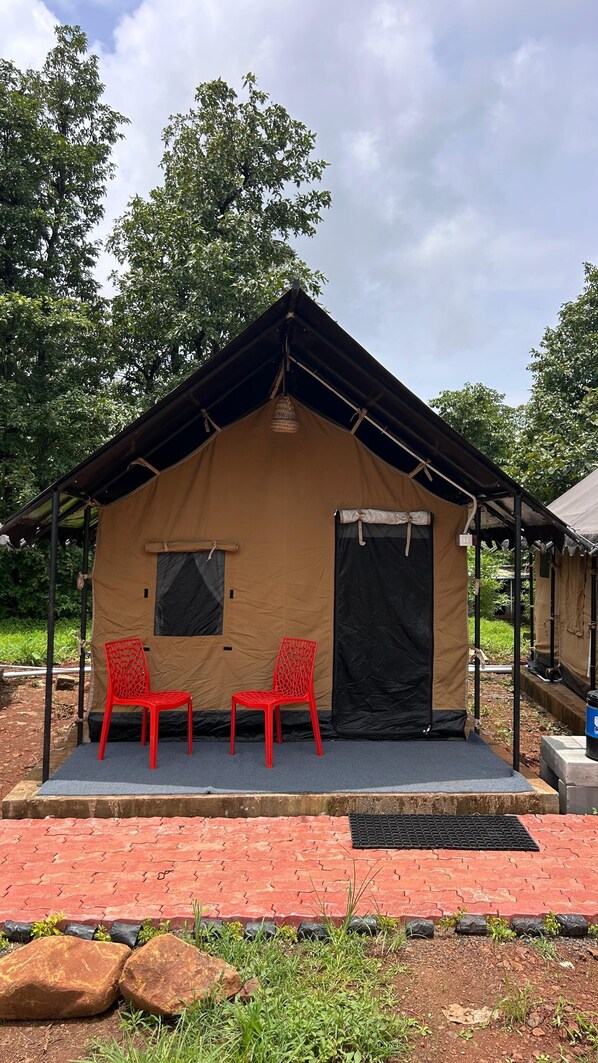 Una piccola tenda singola con tetto, due sedie rosse di plastica e una porta nera.