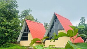 Un edificio moderno con techo rojo y ventanas amplias, rodeado de abundante vegetación.