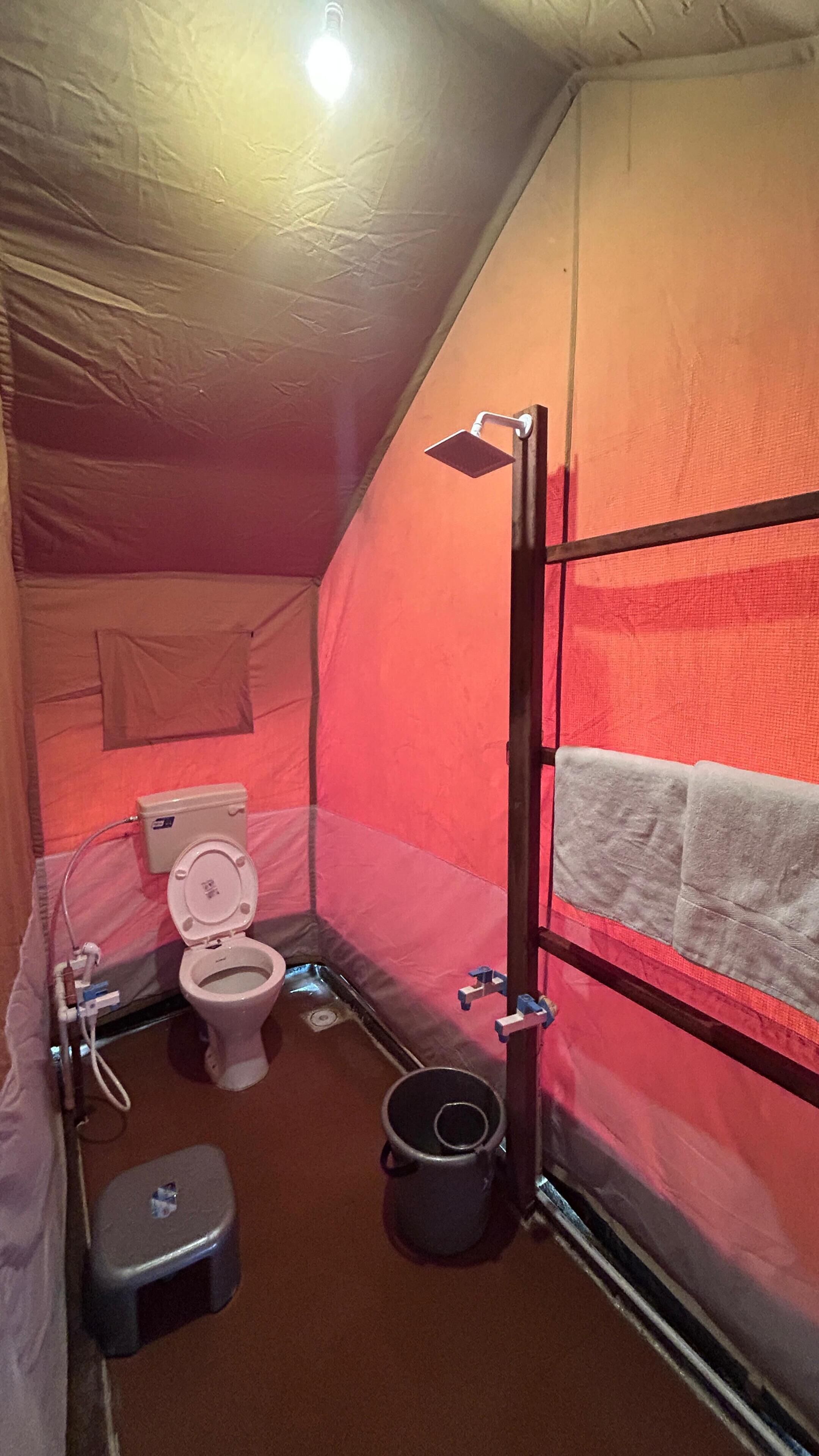 Una carpa con un inodoro, un cubo y una zona de ducha.
