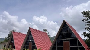 Una hilera de edificios modernos con techos triangulares y grandes ventanales, rodeados de un área ajardinada con árboles jóvenes y un sendero pavimentado.