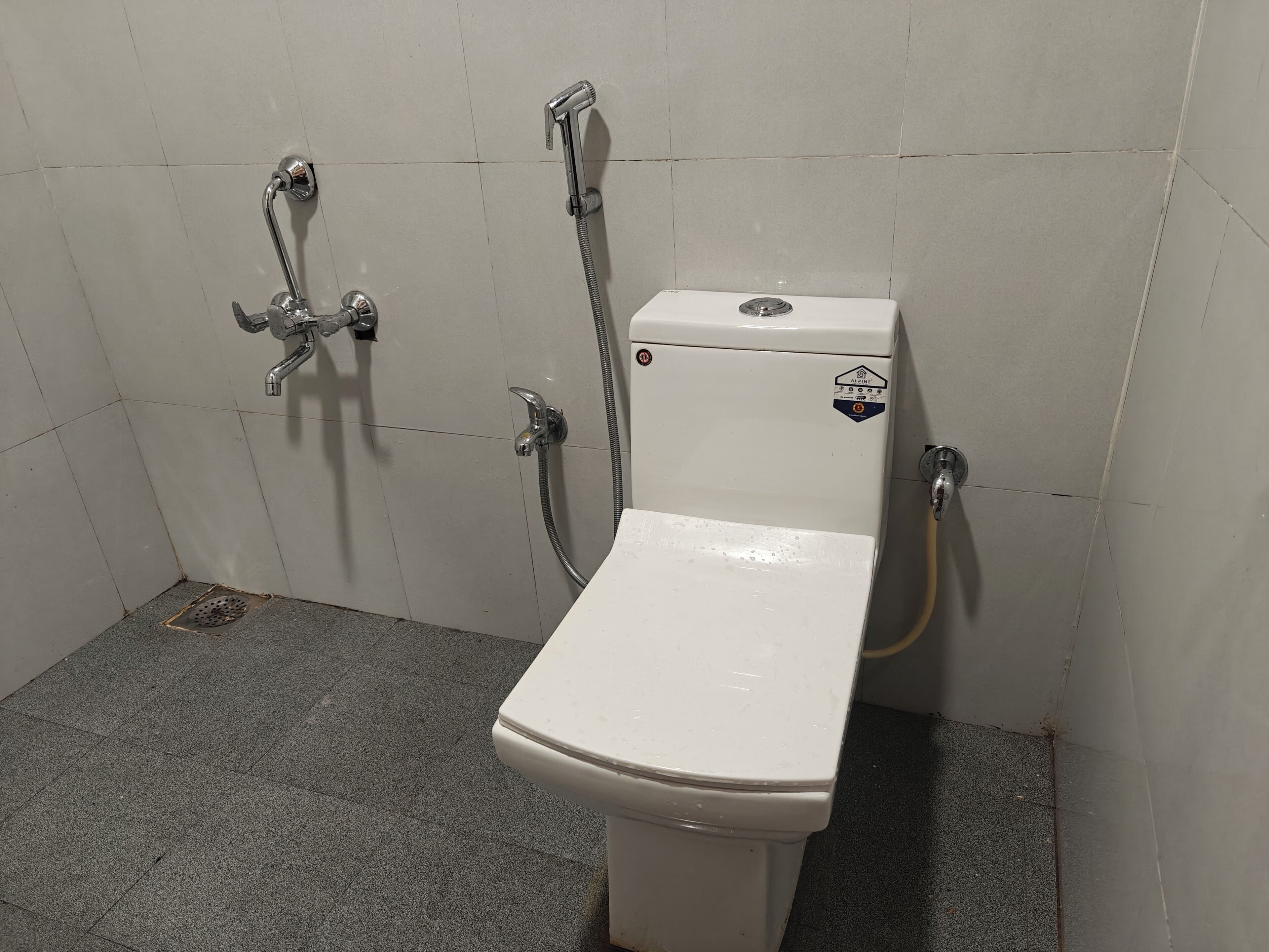Eine weiße Toilette mit Bidet-Ausstattung, einer Duschbrause und einem Wasserhahn an der Wand.