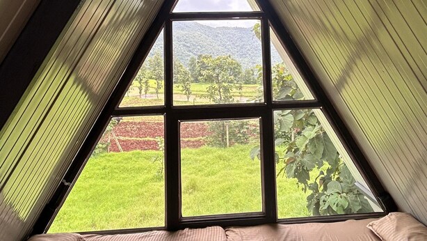 Una habitación con techo inclinado, un ventanal grande y una cama con ropa de cama a rayas.