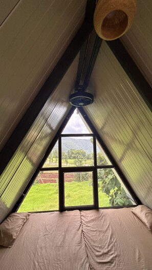 A room with a sloped ceiling, a large window, and a bed with striped bedding. - Huts And Hunters Resort Saputara (Ahwa)
