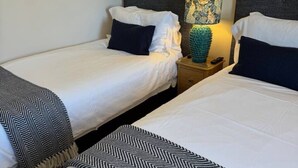 A hotel room with two single beds, each with white bedding and a black and white patterned throw. There is a nightstand with a lamp between the beds.